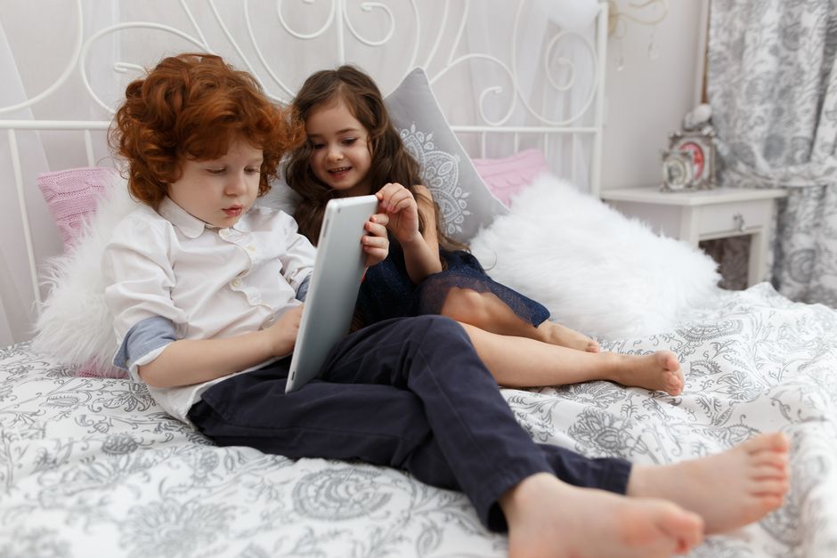 Hai bạn nhỏ nằm trên giường xem máy tính bảng